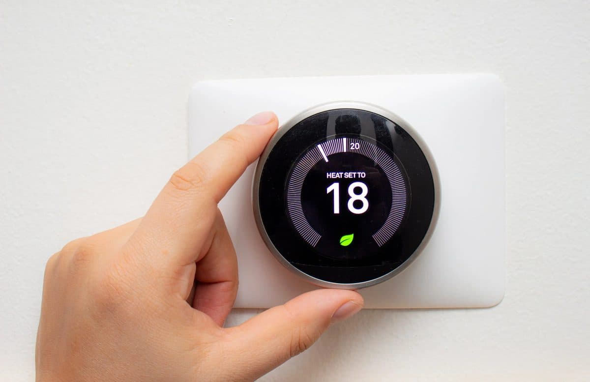 Hand turning the dial of a round smart thermostat mounted on a white wall
